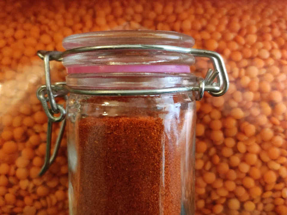 Red lentils in background, small jar of finely ground red peppers in foreground